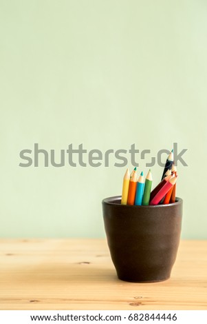 Color pencils in brown ceramic cup on wooden table