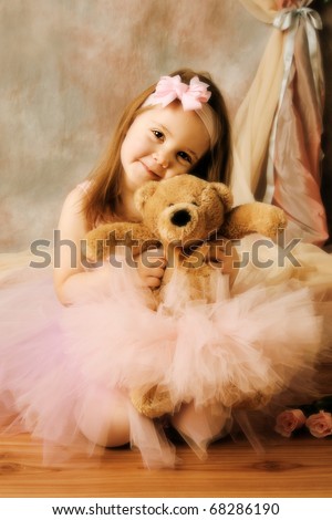 Adorable little girl dressed as a ballerina in a tutu, hugging a teddy bear next to pink roses.
