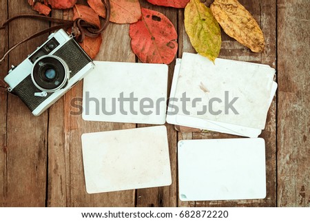 Retro camera and empty old instant paper photo album on wood table with maple leaves in autumn border design - concept of remembrance and nostalgia in fall season. vintage rustic style.