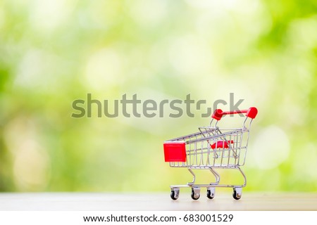 Small model shopping cart on blur green tree leave background. For commerce concept.