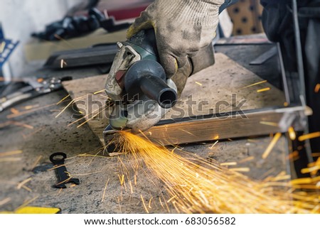 Close up A man welder in a construction gloves, hard works and brews  grinder metal an angle grinder   in the   garage on a wooden table