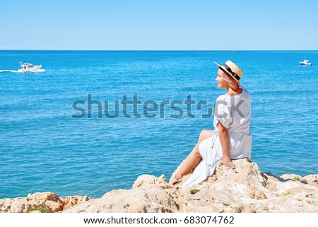 Beautiful girl in a summer dress and hat on the seashore near a background old city europe. Mediterranean Sea, Sitges, Spain.