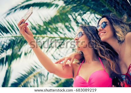 Friends taking selfie at beach, palm tree at background
