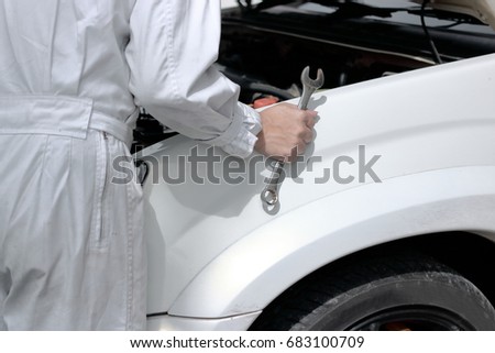 Side view of automotive mechanic in uniform with wrench diagnosing engine under hood of car at the repair garage.