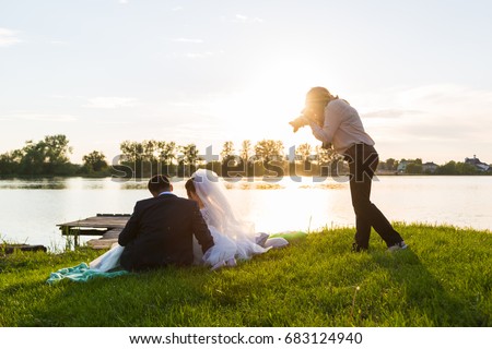 Wedding photographer photographs brides sitting on the lake. Sunset, the sun shines in the camera.