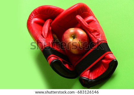 Pair of leather boxing sportswear with juicy red apple. Knock out and healthy nutrition concept. Sport equipment and fruit on light green background. Boxing gloves in red color