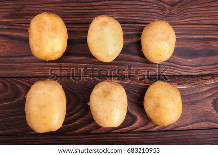 Close-up of a lot of raw, organic, fresh and young potatoes on a dark brown wooden background. Harvest of new potato tuber. Human health staple food, potatoes. Summer vegetables, top view.