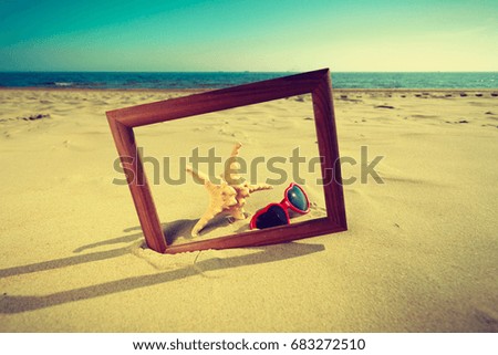 Summer photos concept. Frame on sand on the beach. Seashells and sunglasses lying on the seashore by the sea. 