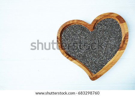 Wooden brown heart bowl full of chia seeds on white wooden background. Text space. Top view.