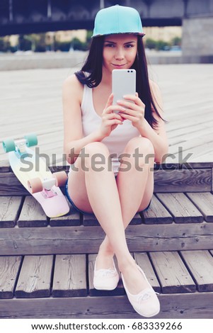 Cute young brunette girl takes mobile photo with smart phone. Attractive female model with modern cellphone takes picture
