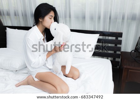 Young Asian woman playing puppy doll on the bed in morning bedroom, alone and lonely
