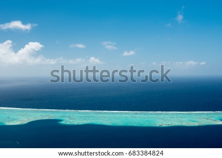Aerial view on lagoon of Raiatea island in French Polynesia with blue and turquoise water, barrier reef, blue sky and white clouds 