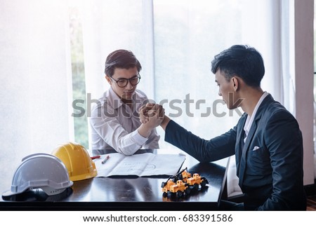 Two engineers are arm wrestling to demonstrate high competition in work. Business real estate concepts are high risk.