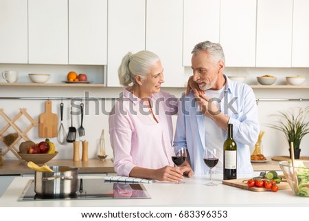 Image of mature happy loving couple family standing at the kitchen drinking wine. Looking aside.
