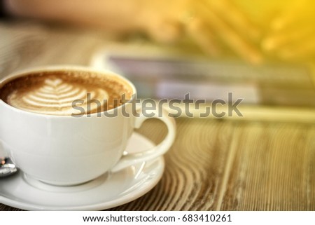 cup of coffee on a wooden table on a background of young woman works with digital tablet