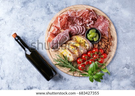 Set of meat antipasti served with herbs, almonds, tomatoes and olive oil on rustic wooden board over a stone background. Top view