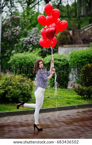 Portrait of a gorgeous beautiful bridesmaid in a pretty dress holding heart-shaped red balloons in the park at bachelorette party.