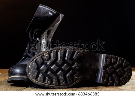 Old black Polish military boots on a wooden table. Black background.