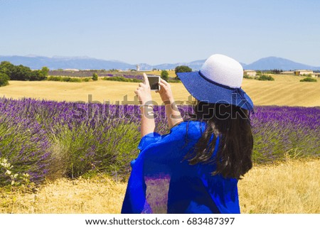 A girl in a hat is photographing of a lavender field in France on the phone.