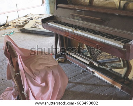 Brown Grand piano with the lid open and the chair in the room among the dust, dirt and debris in an abandoned theater.