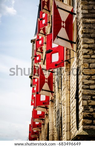 Portrait format picture of the wall of a castle made of brownish bricks in medieval style with many opened wooden window shields painted in red and white, photo captured in The Netherlands.