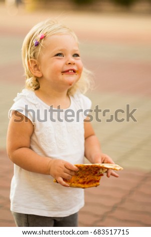 A little girl is eating a large slice of pizza, getting dirty. Vertically.