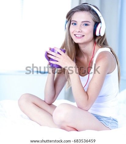 Portrait of beautiful woman in morning listening music sitting on bed at home