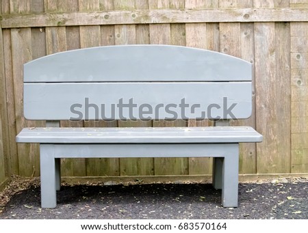 Lonely single park bench in front of plain wooden fence Royalty-Free Stock Photo #683570164