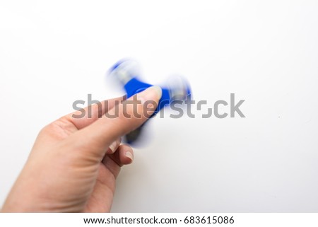 Hand playing with a bkue spinner. Stress relieving toy on white background. Close-up. Top view. Nobody. Stock photo