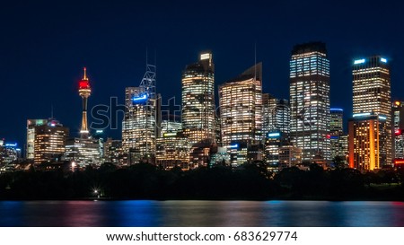 Beautiful illuminated Sydney CBD Skyline in the evening with reflections in water at Farm Cove Bay in long exposure photography.