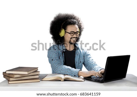 Picture of an Afro male college student is listening to music with a headphone while studying with a laptop and books