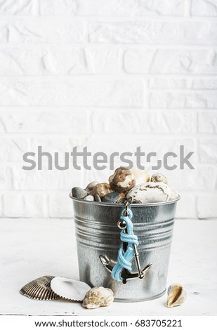 Interior pail full of sea stones for decoration or hand-made articles in marine style with a silver decorative anchor on a white brick wall background. Selective focus