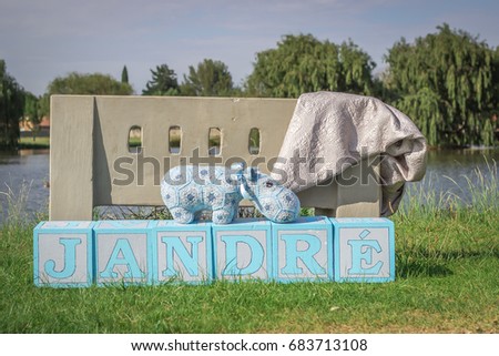 Baby's name spelled in large blue toy blocks with park bench and hippo teddy bear at lake
