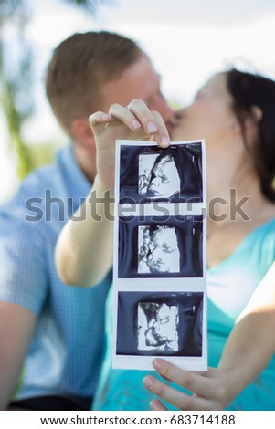 Pregnant couple kissing holding up baby ultrasound pictures