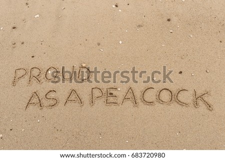 Handwriting  words "PROUD AS A PEACOCK" on sand of beach.