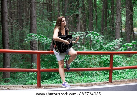Woman with a guitar and backpack in a road trip with forest view