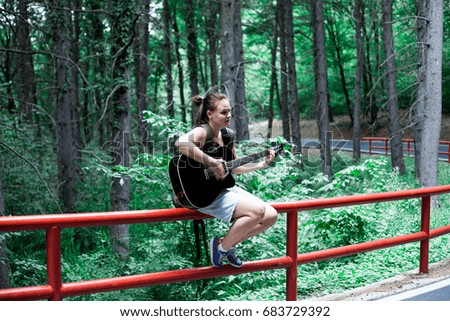 Woman jamming in a forest on a road side on a black acoustic guitar