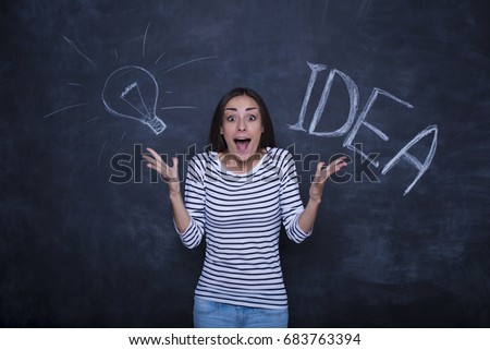 Happy young woman on light bulb drawn on blackboard background above her 