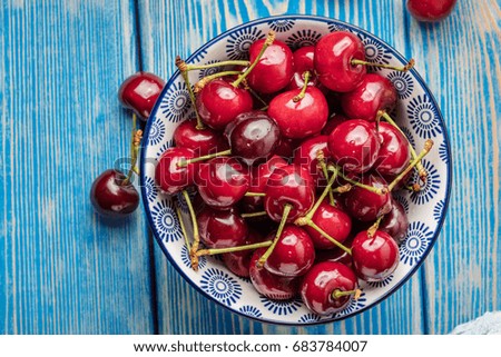 Fresh cherries in a blue bowl on a blue wooden table. Small depth of field. Top view.