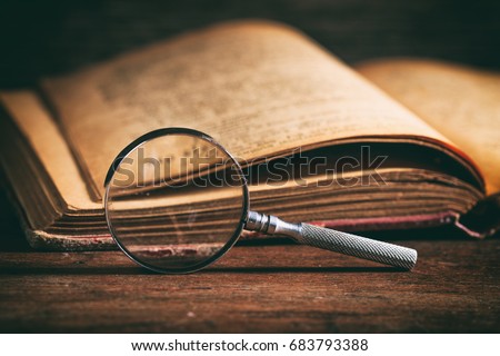 Vintage book and magnifying glass on wooden background
