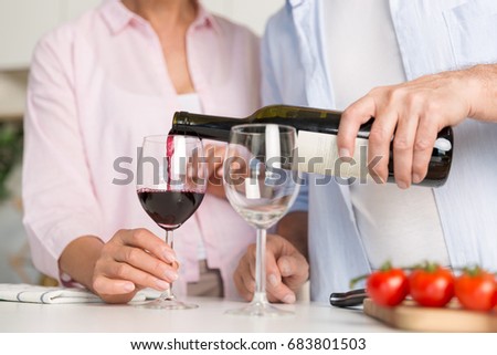 Cropped picture of mature loving couple family standing at the kitchen drinking wine