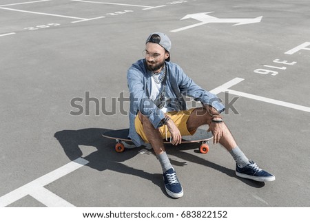 stylish young caucasian man sitting on longboard on street