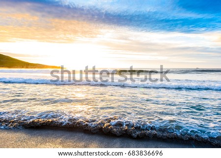 Small ocean sea waves on sandy beach with sunrise sunset. Background landscape picture of dusk or dawn at the Atlantic ocean beach with small waves at low tide. Background wallpaper picture.