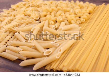 Close-up picture of different types and shapes of Italian pasta on a table. Assorted types of pasta: maccheroni, fusilli, penne and farfalle. Flour products.