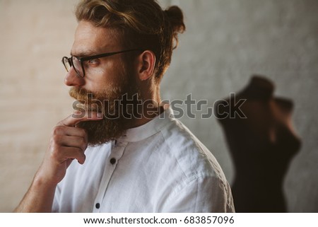 Side view of bearded blonde man wearing glasses white shirt touching chin with mock-up on background.