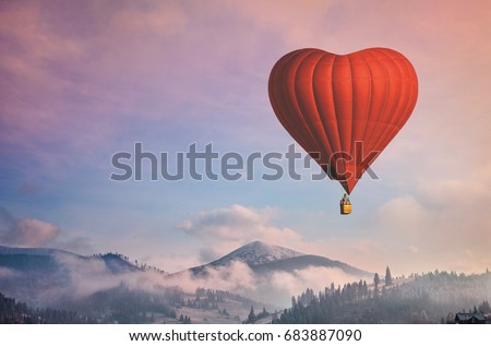 Beautiful red air balloon heart shape against blue and pink pastel sky in a sunny bright morning. Foggy mountains in the background. Romantic trip on Valentine's Day. Sport and recreation travel theme