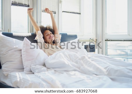 Woman stretching in bed with her arms raised Royalty-Free Stock Photo #683927068