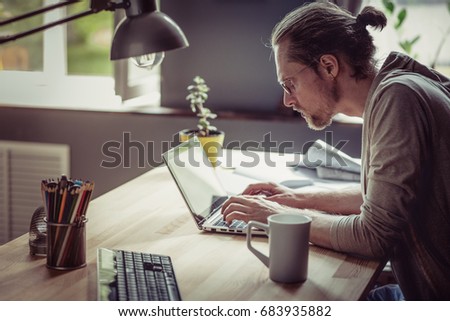 Freelancer typing and working with laptop. Man working on freelance at home seriously looking in computer.