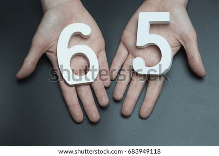 On a black background, female hand with the number sixty-five.
