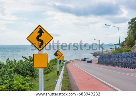 Yellow sign with winding road symbol in the countryside sea and sky background .